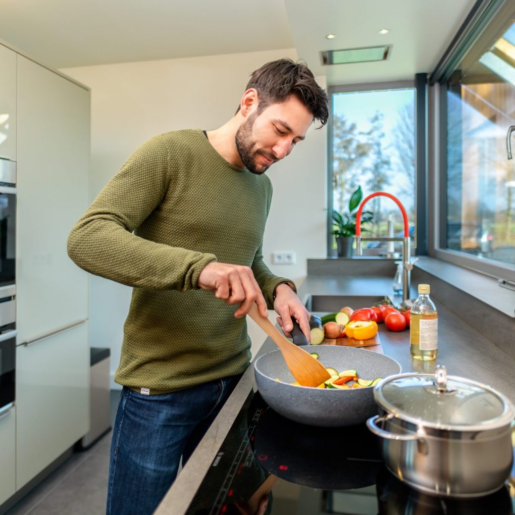 Man die staat te koken in een moderne keuken en groente roerbakt in een wokpan.