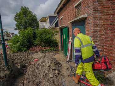 Man in gele werkkleding loopt met gereedschapstas in zijn hand langs werkzaamheden bij een elektriciteitsstation